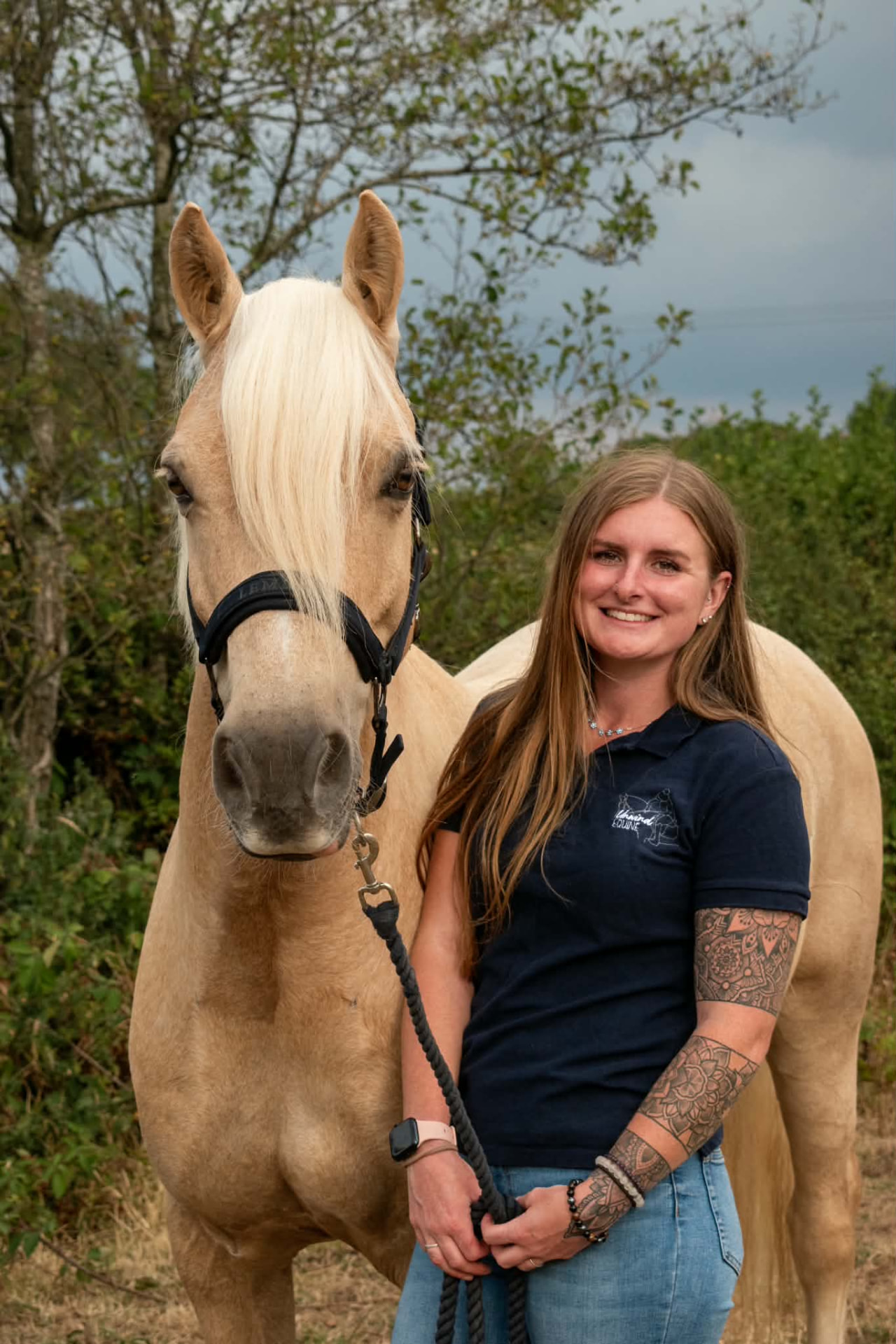 Jess smiling beside a palomino horse on a summer evening